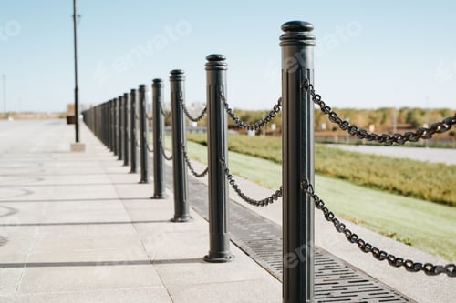 Preview: Black iron fence posts with chain. Decorative fence pillar outdoors on a sunny day, perspective view