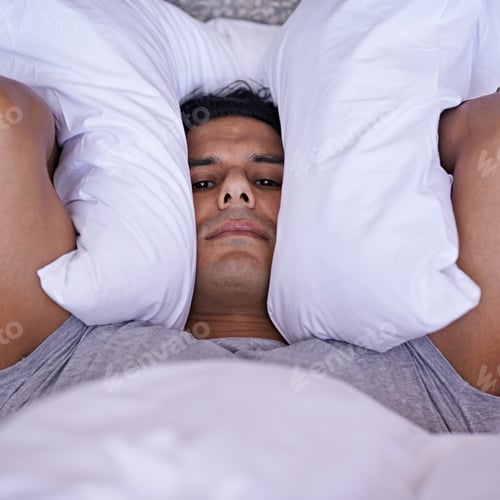 Preview: No-one can sleep with all this noise. A young man covering his ears with his pillow.
