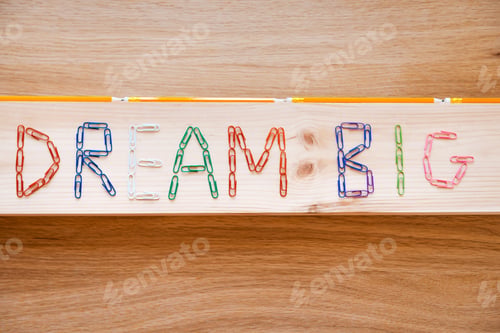 Preview: Dream big. Top view of dream big text made from colorful staples laying on the wood grain