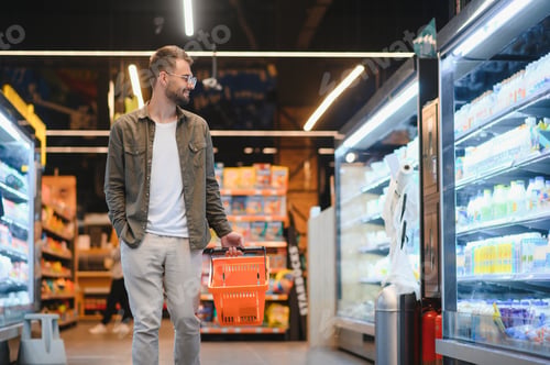 Preview: Portrait of smiling handsome man grocery shopping in supermarket, choosing food products from shelf