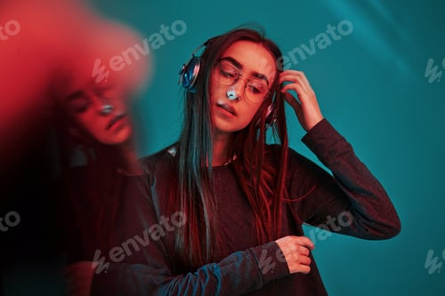 Preview: Quality music in headphones. Studio shot indoors with neon light. Portrait of beautiful young girl