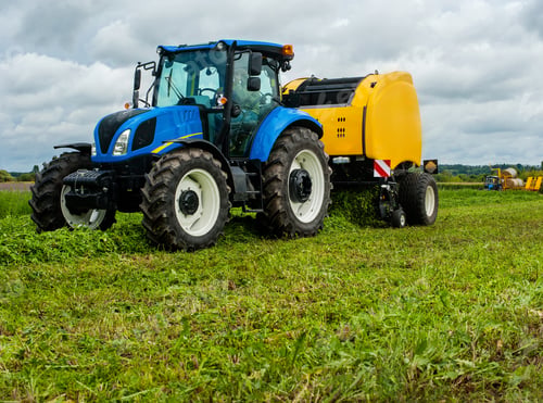 Preview: new blue tractor with baler in motion on farmland with cloudy sky