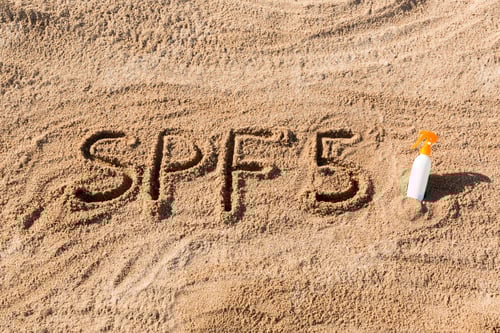 Preview: Sun protect factor five. SPF 5 word written on the sand and white bottle
