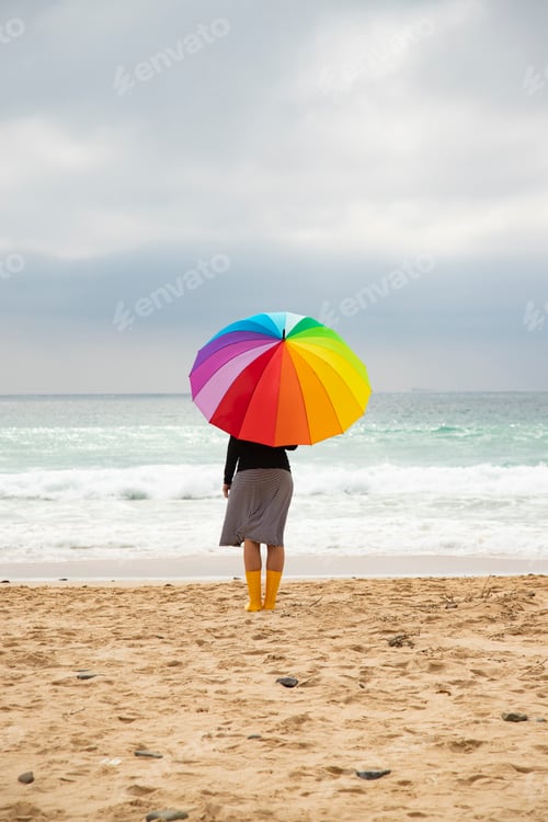 Preview: Woman with colorful umbrella sitting on the beach