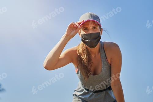 Preview: Female jogger running in mask in the countryside