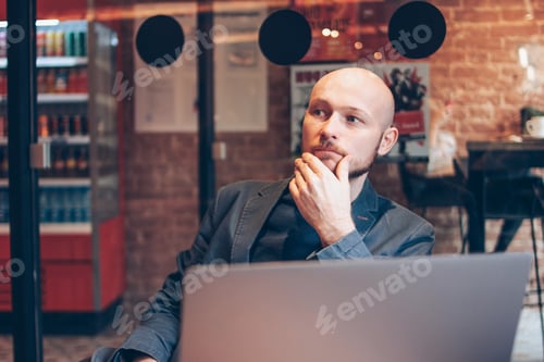 Preview: Thinking attractive adult successful bald bearded man in suit with laptop in cafe