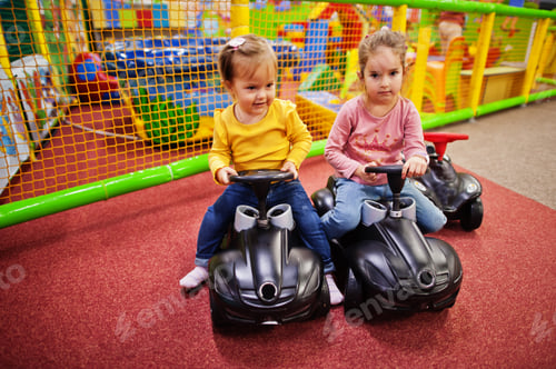 Preview: Two siters rides on a plastic cars in indoor play center.