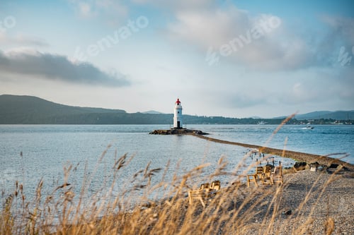 Preview: Sea autumn landscape. An old lighthouse with a red roof on a pebble beach.