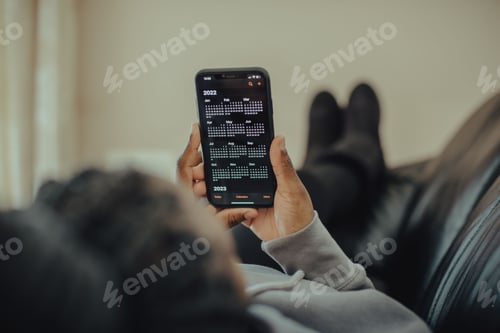 Preview: Young female holding her smartphone with a calendar on a desk