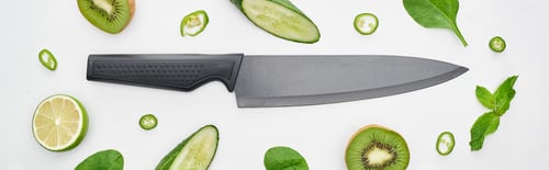 Preview: panoramic shot of knife, fresh cucumbers, kiwi, lime, peppers and greenery