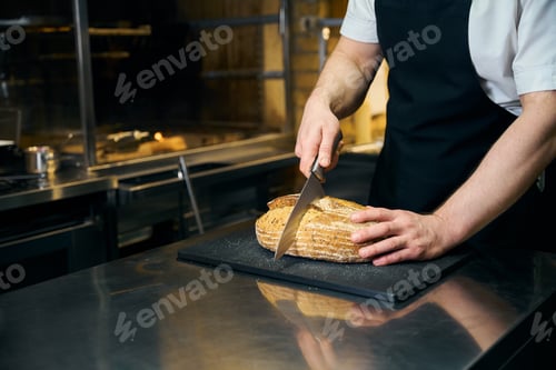 Preview: Partial male chef cutting bread with knife on chopping board on blurred kitchen
