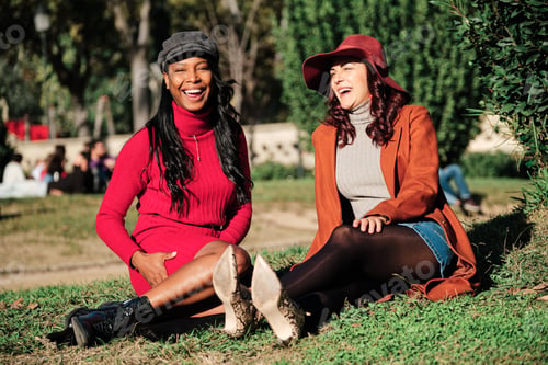 Preview: Stylish multiethnic friends sitting on a park under the sun