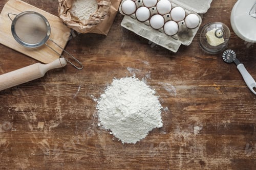 Preview: top view of white flour pile and baking ingredients on wooden table