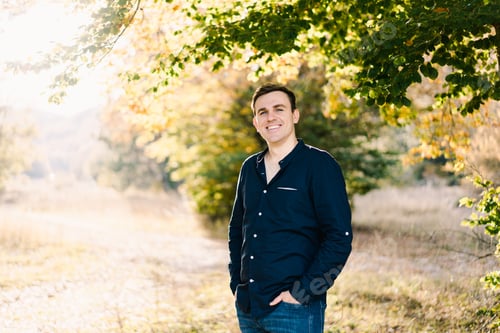 Preview: Smiling man standing on the sunny lawn near a tree
