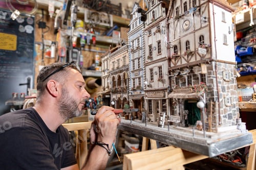 Preview: Modeller man working at scale model of miniature building in his workshop full of tools
