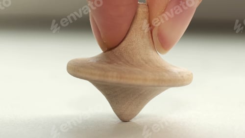 Preview: wooden toy spinning top is spinning on a white table. The top slows down, losing balance or
