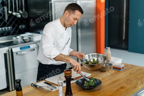 Preview: Professional kitchen chef puts salad leaves with pear and cheese on a plate with tongs