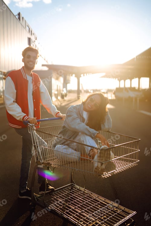 Preview: Stylish man and woman having fun and riding shopping cart. Lifestyle, leisure, youth concept.