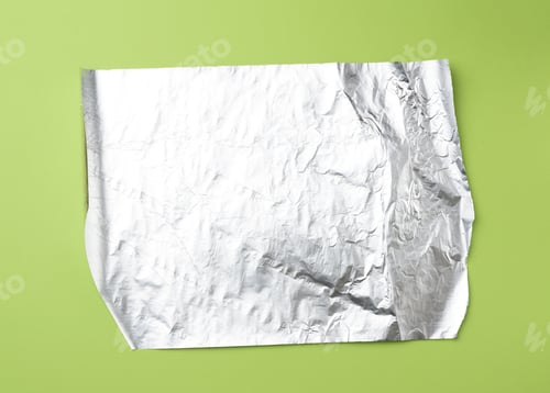 Preview: Gray foil for baking and packaging food on a green background, top view