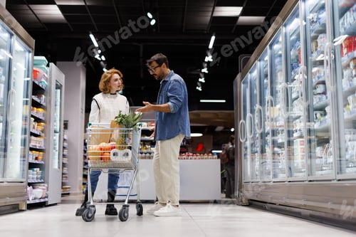 Preview: Couple discussing shopping list while grocery shopping in supermarket