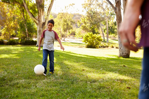 Preview: Seven year old boy playing football in a park with dad