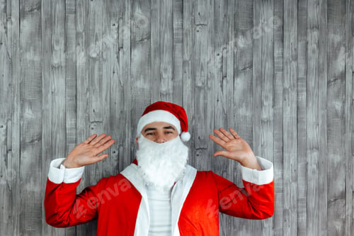 Preview: Caucasian young man dressed as papa noel with hands up. Copy space on top
