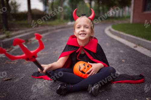 Preview: Little caucasian Girl in costume of devil with pumpkin jack lantern celebrating Halloween outdoor