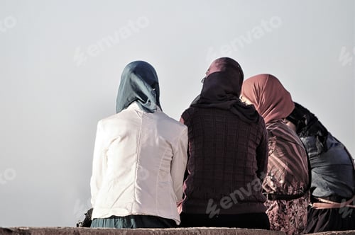 Preview: Group of women with colorful hijabs sitting on a bench and talking under a grey sky