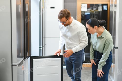 Preview: shop assistant demonstrates refrigerator to young woman in home appliance shopping mall supermarket