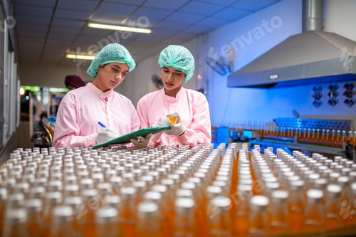 Preview: Asian woman worker with clipboard is checking product bottles of fruit juice on the production line.