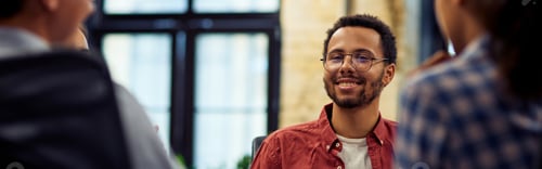 Preview: Young smiling mixed race male office worker sitting at the desk and talking with colleagues
