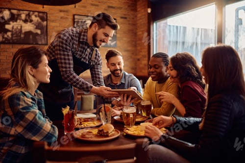 Preview: Happy waiter using touchpad while showing the menu to group of guests in a pub.