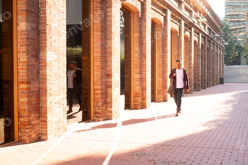 Preview: Young man walking through brick corridor in sunlight