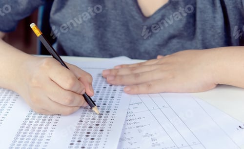 Preview: Students hand holding pencil writing selected choice on answer sheets