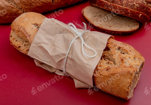 Preview: side view of crispy baguette with sliced rye bread on bordo background