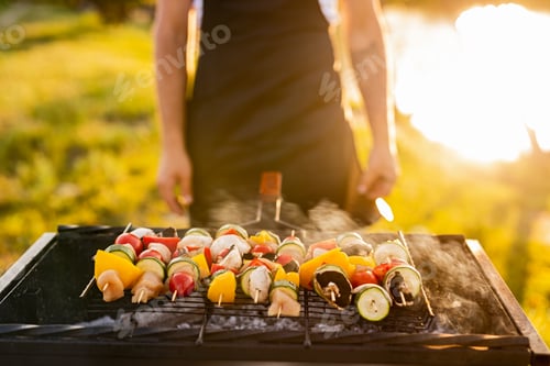 Preview: Crop man roasting vegetable kebabs on grill near lake