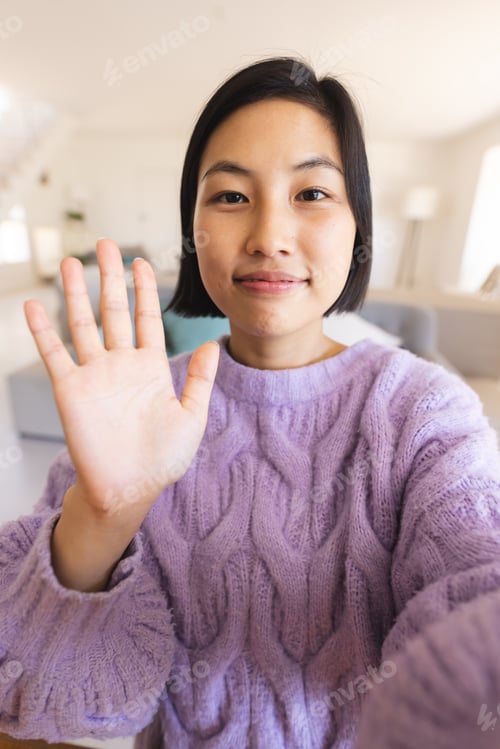 Preview: Happy asian woman sitting at table and having video call, waving to camera