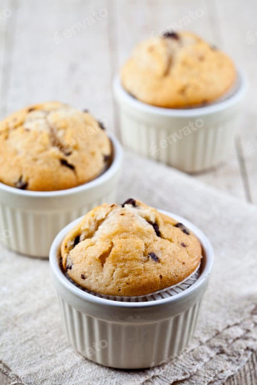 Preview: Homemade fresh muffins on ceramic white bowls on linen napkin on rustic wooden table.