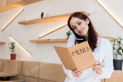 Preview: young beautiful woman talking by phone and looking at menu