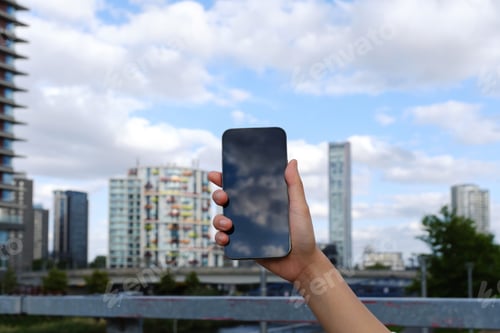 Preview: Hand holding a cell phone while looking at the city in the background