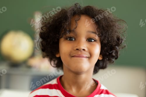Preview: Front view of a Mixed-race schoolboy looking at camera in a classroom at elementary school