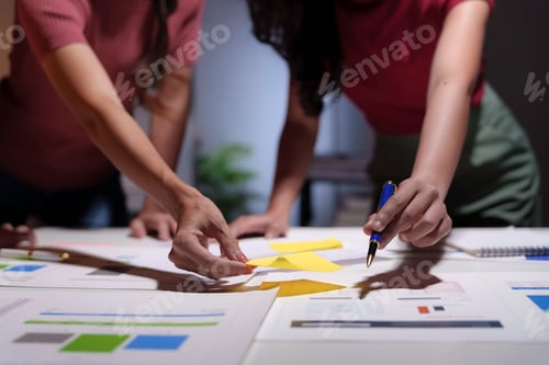 Preview: Two businesswomen are working late at night, using sticky notes and a pen to plan a project