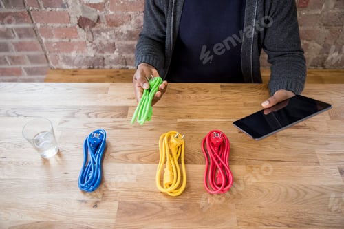 Preview: Businessman with tablet choosing from coloured power cables on table top, partial view
