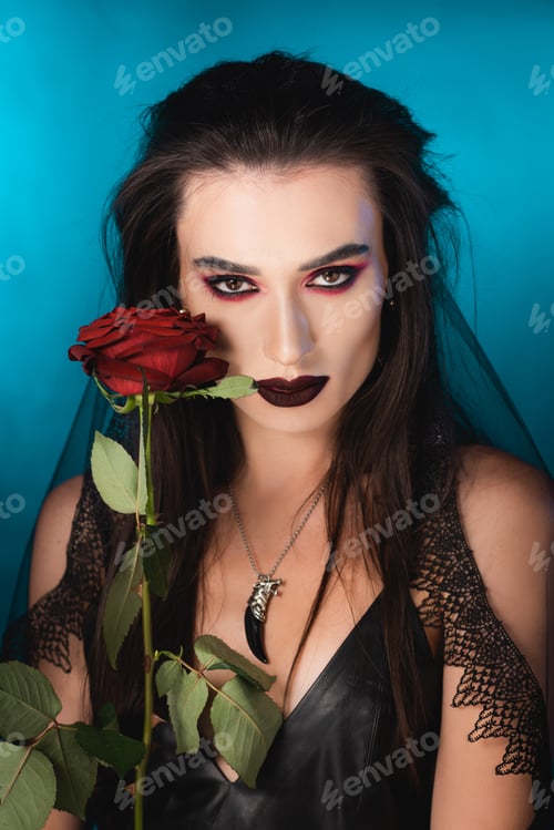 Preview: young brunette woman with dark makeup near red rose on blue