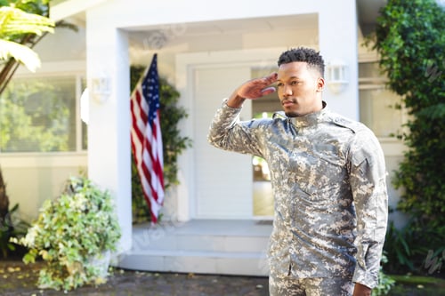 Preview: Focused african american male soldier standing and saluting outside home with usa flag, copy space