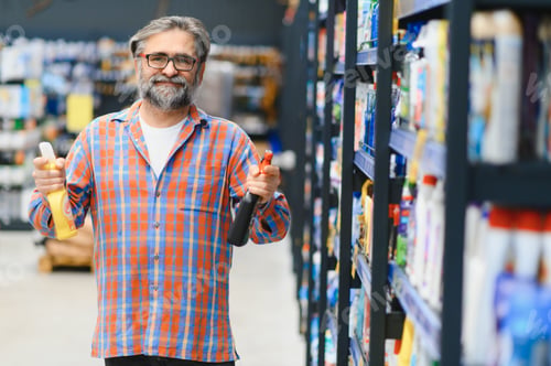 Preview: Portrait of focused man buying household chemicals in supermarket, reading labels on bottles
