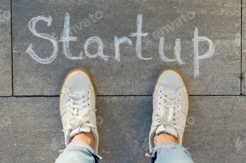 Preview: View from above, female feet with text startup written on grey sidewalk