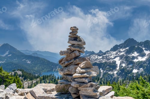 Preview: Mountain peak cairns. Stacked rocks trail marker with beautiful forest and lakes below.