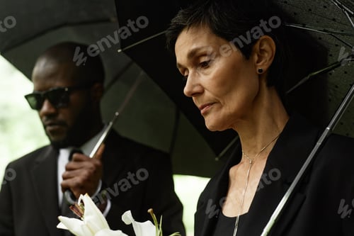 Preview: Senior Woman Looking down on Grave Grieving under Umbrella at Cemetery
