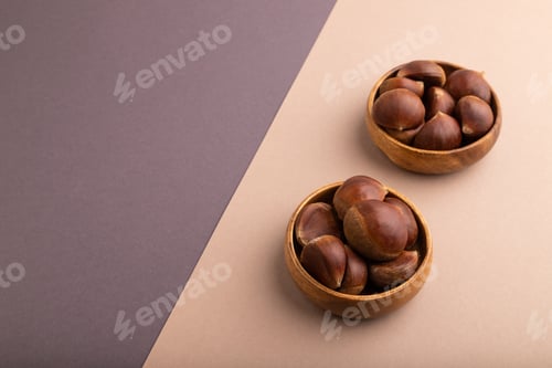 Preview: wooden bowl with raw edible Сhestnuts on brown and gray paper pastel, copy space